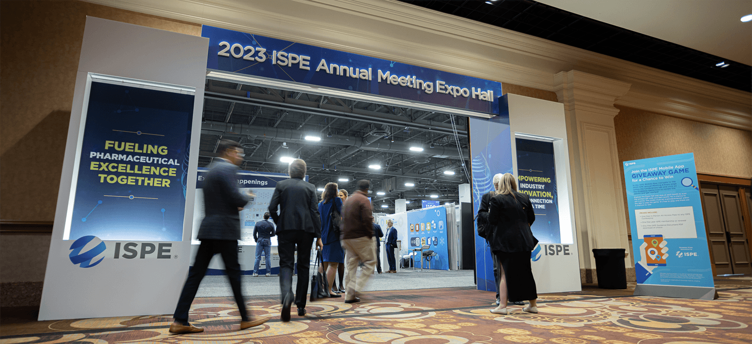 Entrance to the ISPE Annual Meeting Expo Hall. Large signage above the doorway reads '2023 ISPE Annual Meeting and Expo Hall,' with flanking banners displaying motivational text and the ISPE logo as attendees walk in.