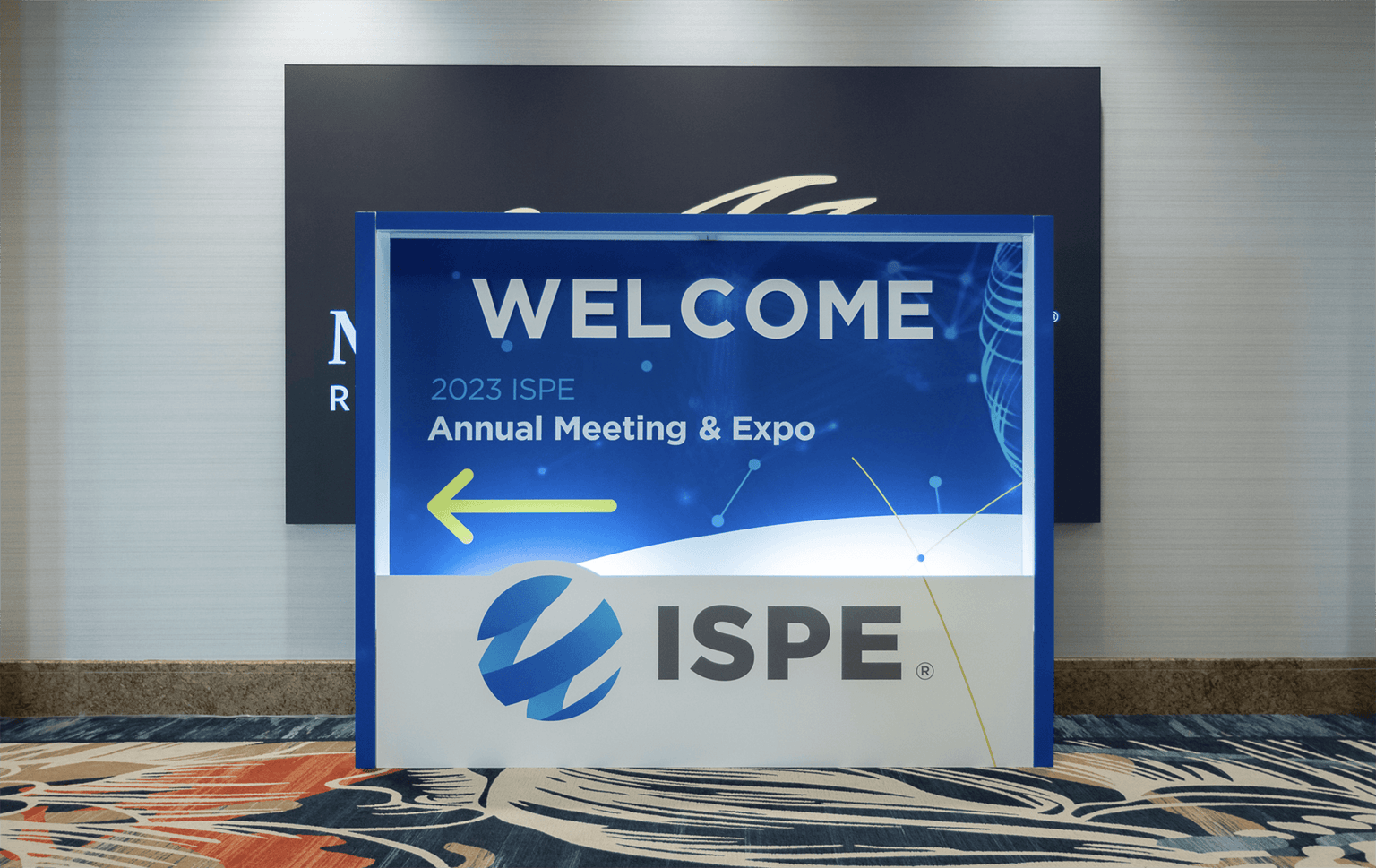 Freestanding welcome sign for the 2023 ISPE Annual Meeting & Expo featuring a bright blue design, large ISPE logo, and a yellow arrow pointing left.